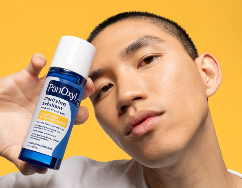 A man holding PanOxyl Clarifying Exfoliant next to his face.