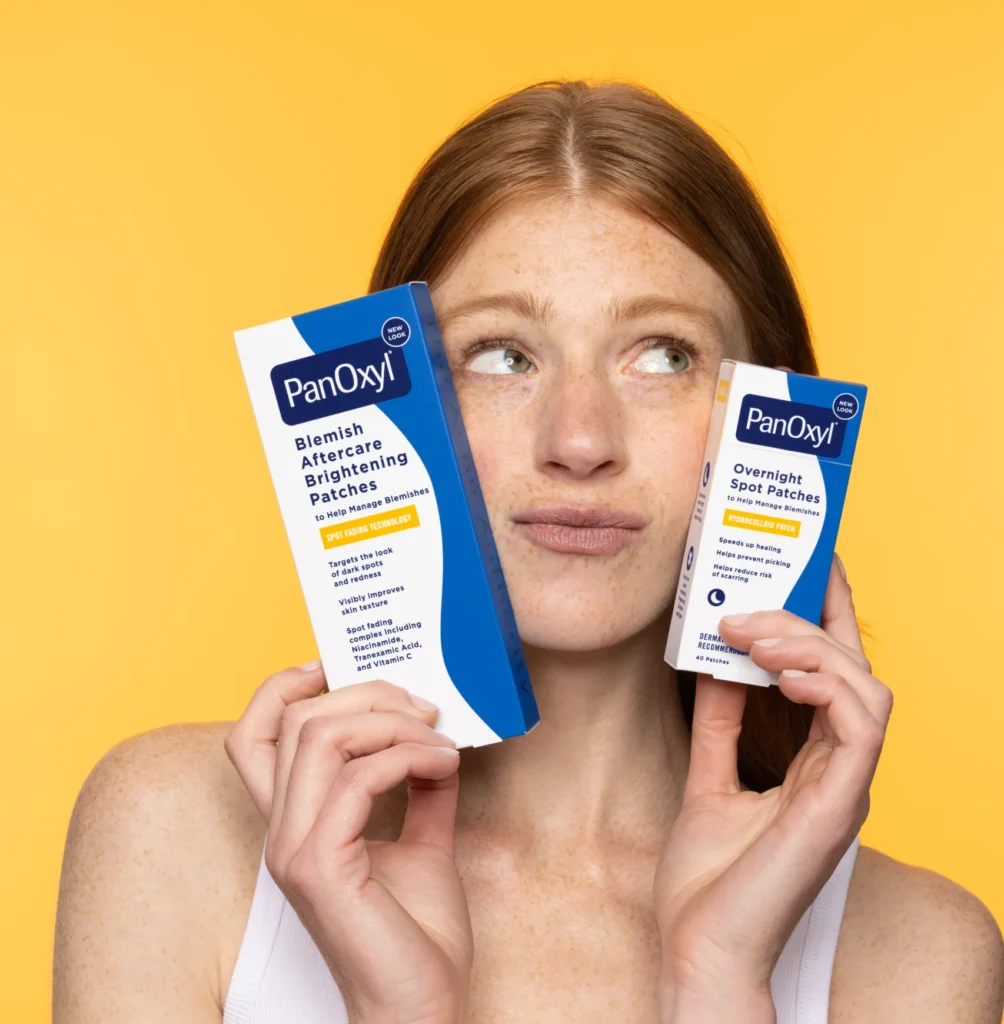 A woman holding PanOxyl blemish aftercare brightening patches and PanOxyl overnight spot patches next to their face.