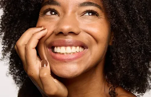 A woman smiling and touching her face.