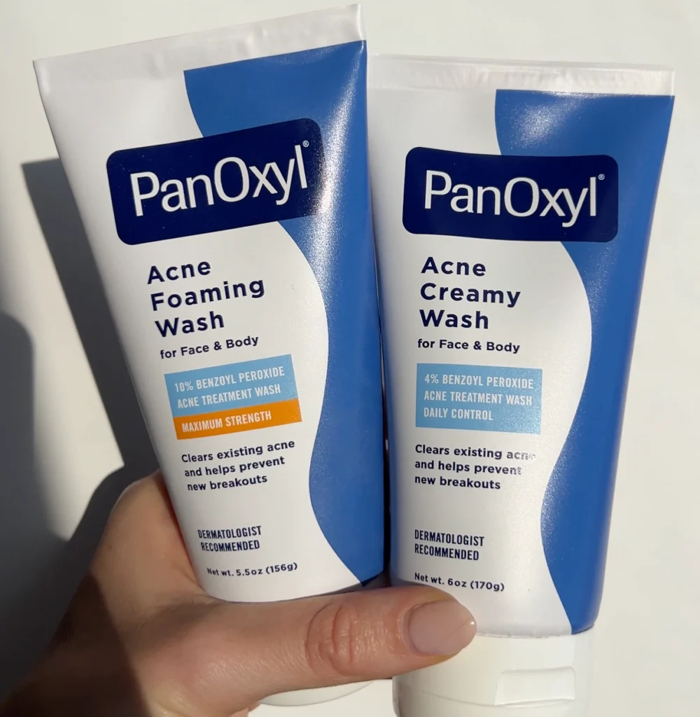 A hand holding PanOxyl acne foaming wash and acne creamy wash.