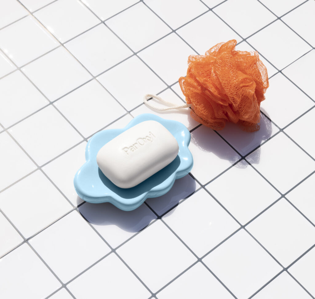 PanOxyl Acne Treatment Bar on a white tile background next to an orange loofah