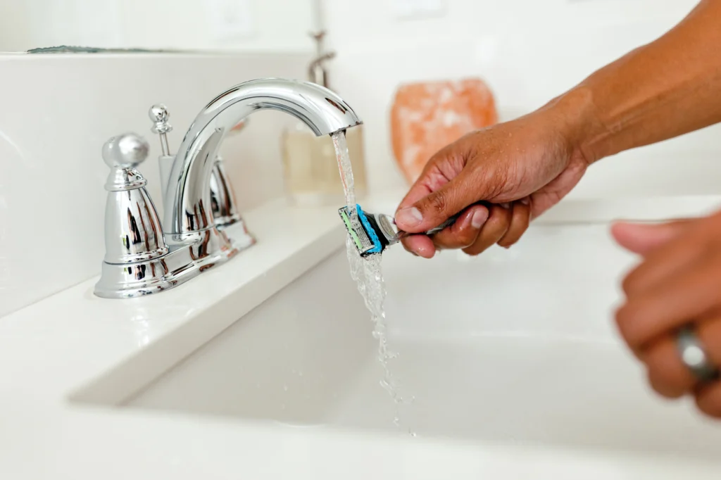 A safety razor being washed under running water.