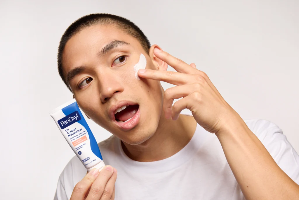 A man putting PanOxyl oil control moisturizer on his face.