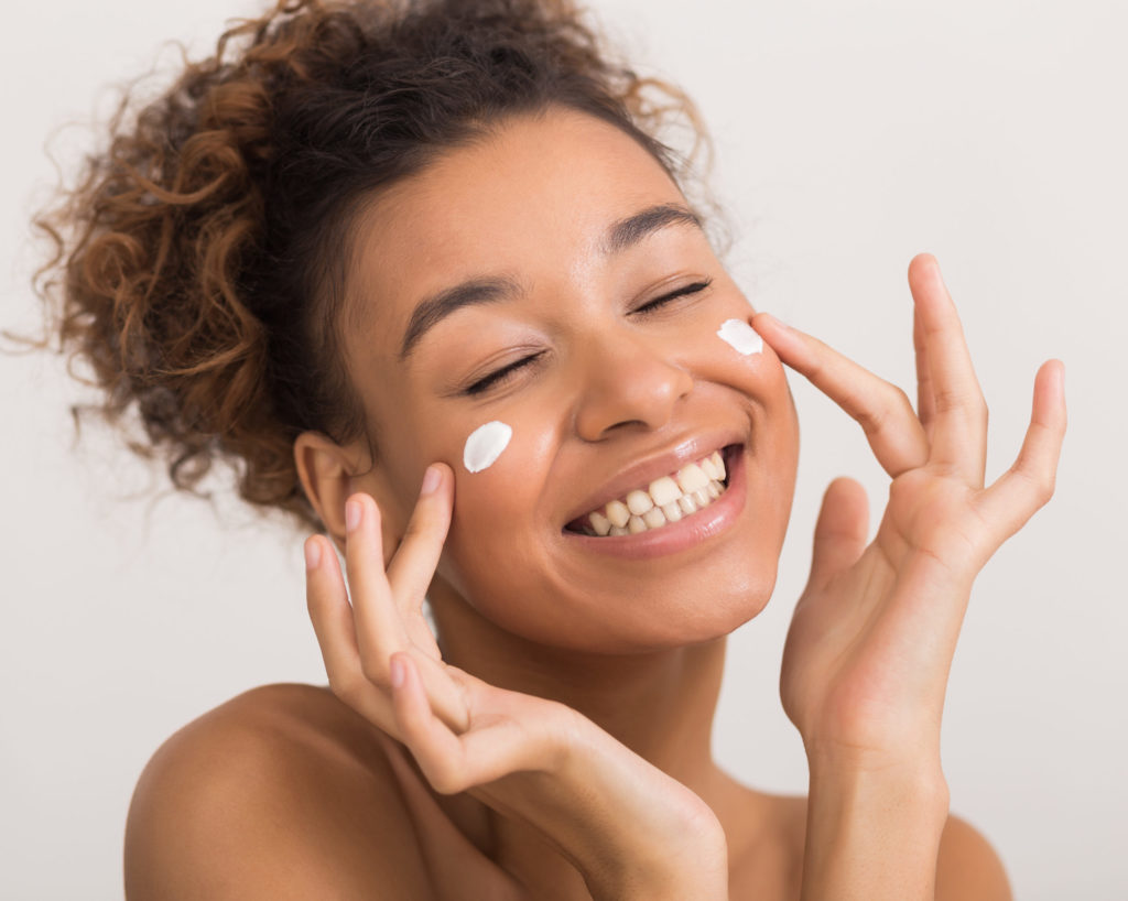 Young woman putting moisturizer on her cheeks
