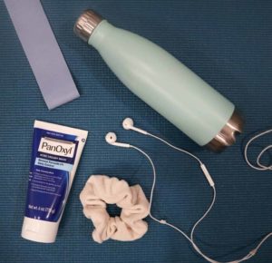 PanOxyl 4% benzoyl peroxide acne wash with a scrunchii, water bottle and earbuds on a workout mat.