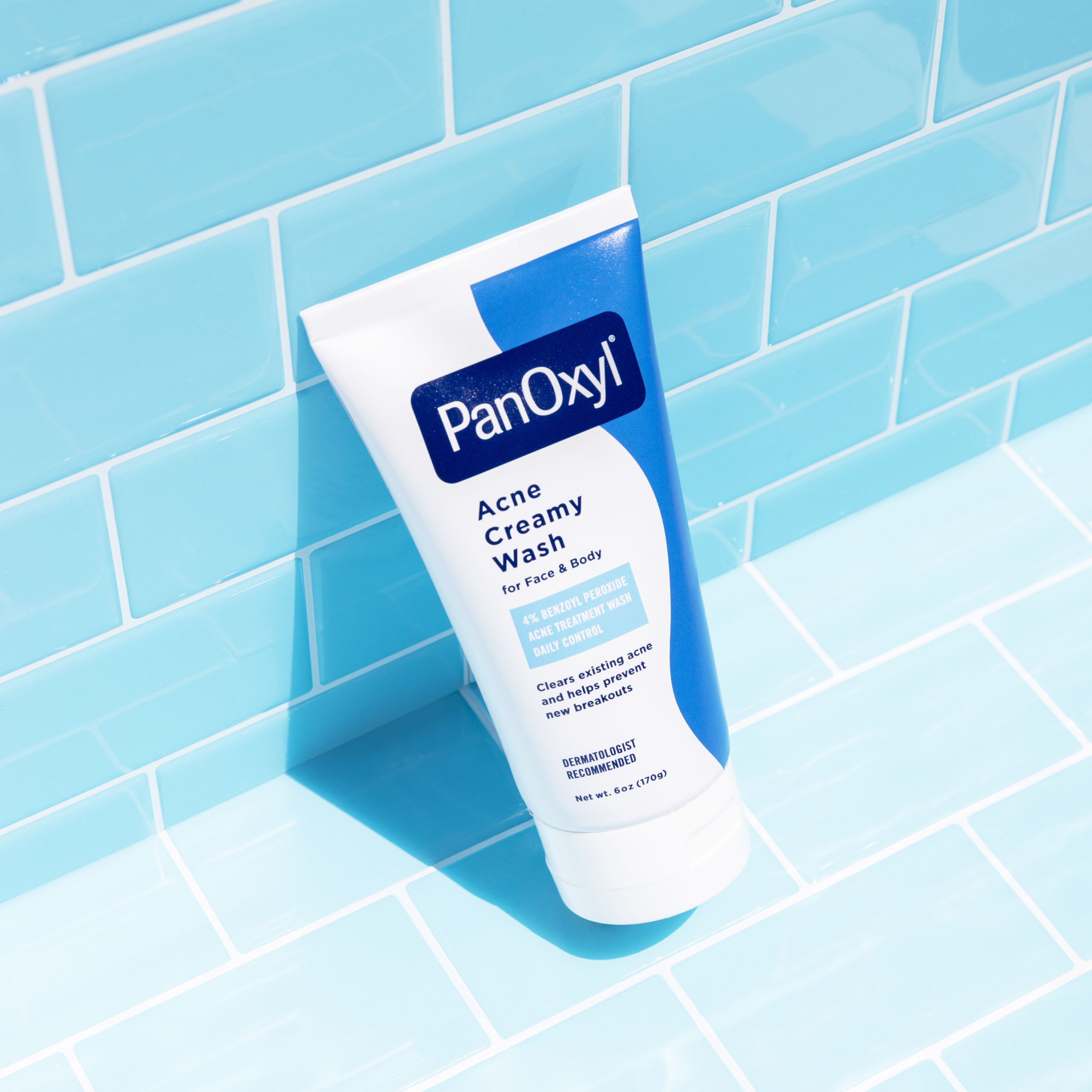 A tube of PanOxyl Acne Creamy Wash on a light blue tiled background