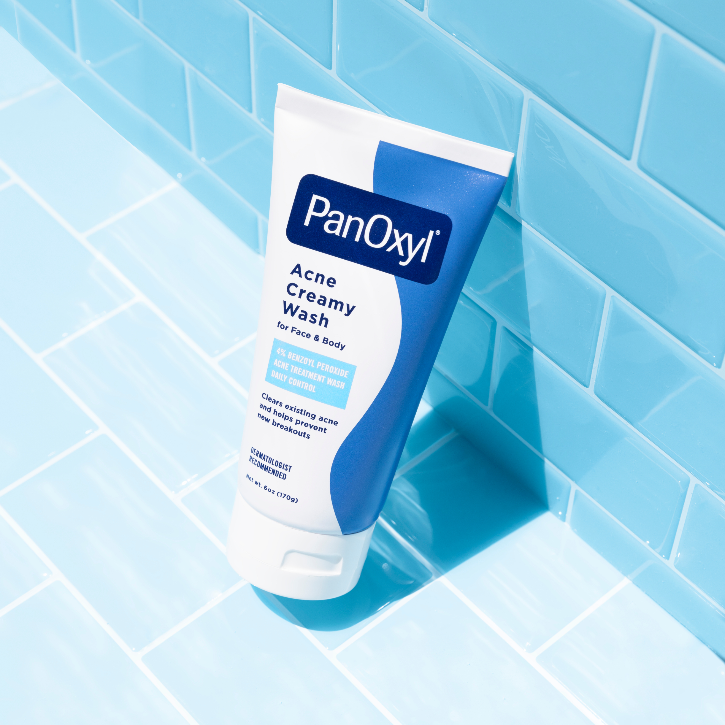 A tube of PanOxyl Acne Creamy Wash on a light blue tiled background