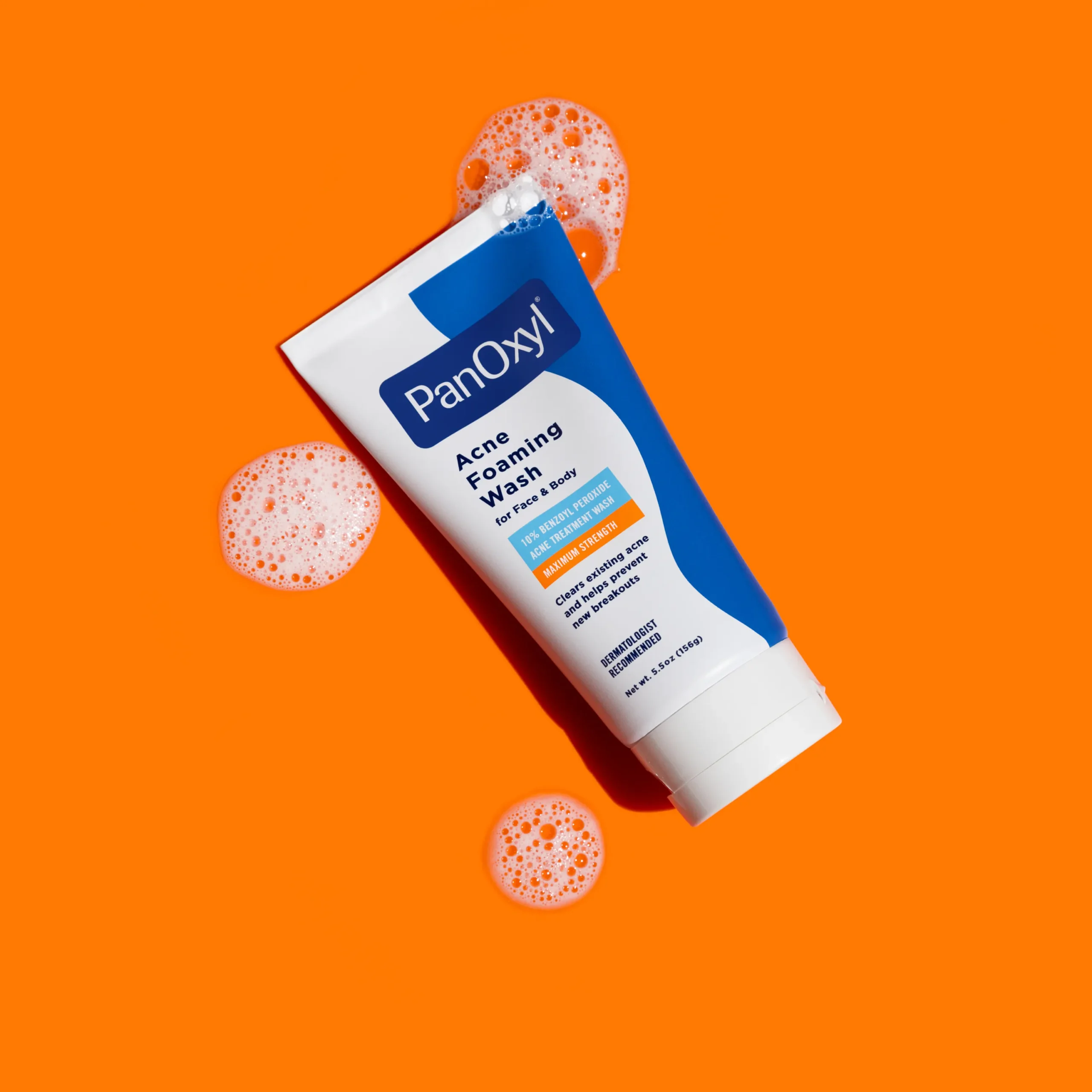 A tube of PanOxyl Acne Foaming Wash with suds around it on an orange background