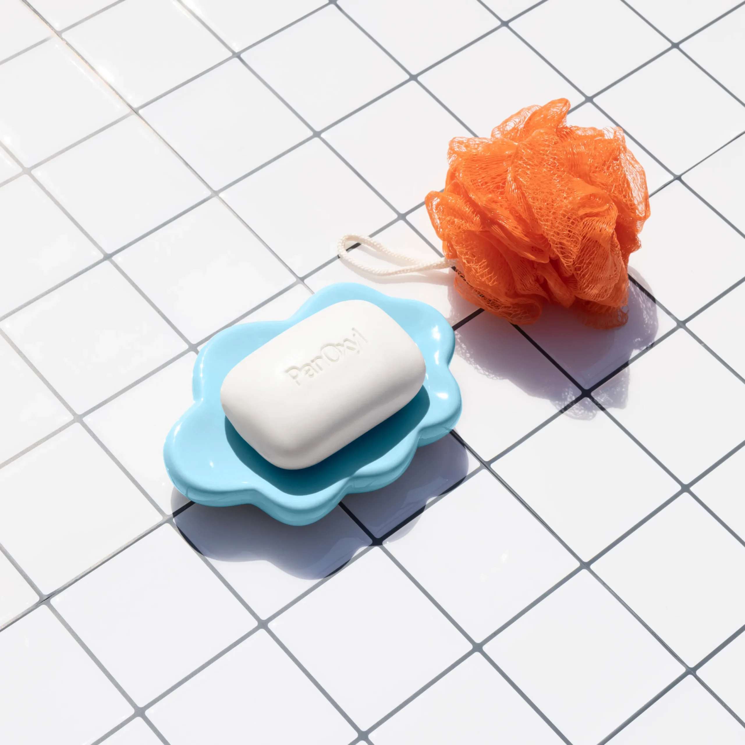 PanOxyl Acne Treatment Bar on a white tile background next to an orange loofah