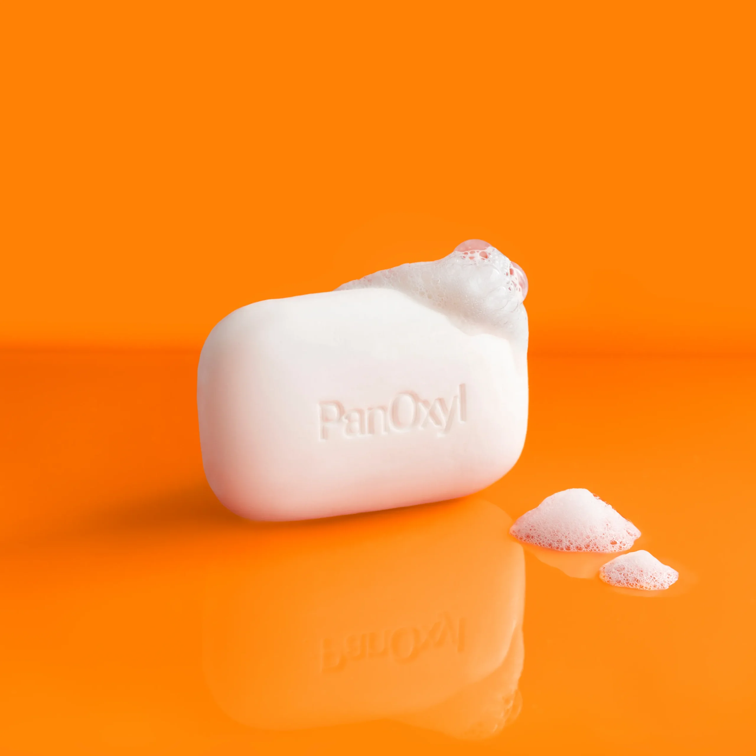 PanOxyl Acne Treatment Bar with Suds on an orange background