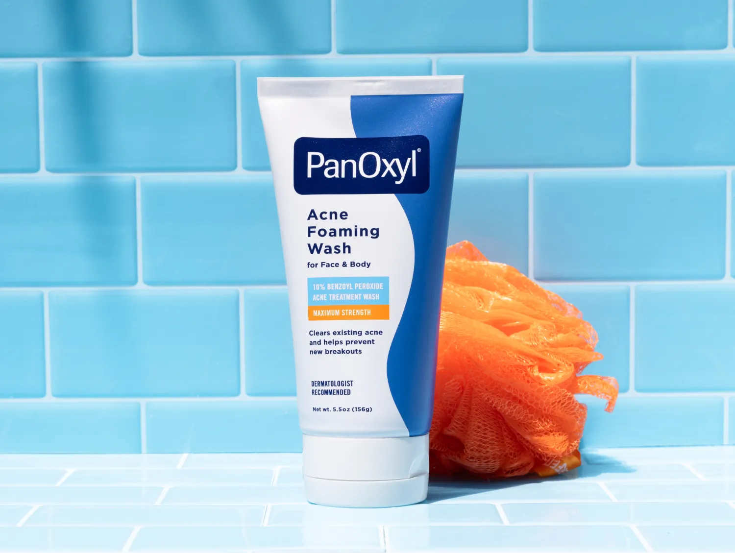 A tube of PanOxyl Acne Foaming Wash on a blue tiled background with an orange loofah next to it