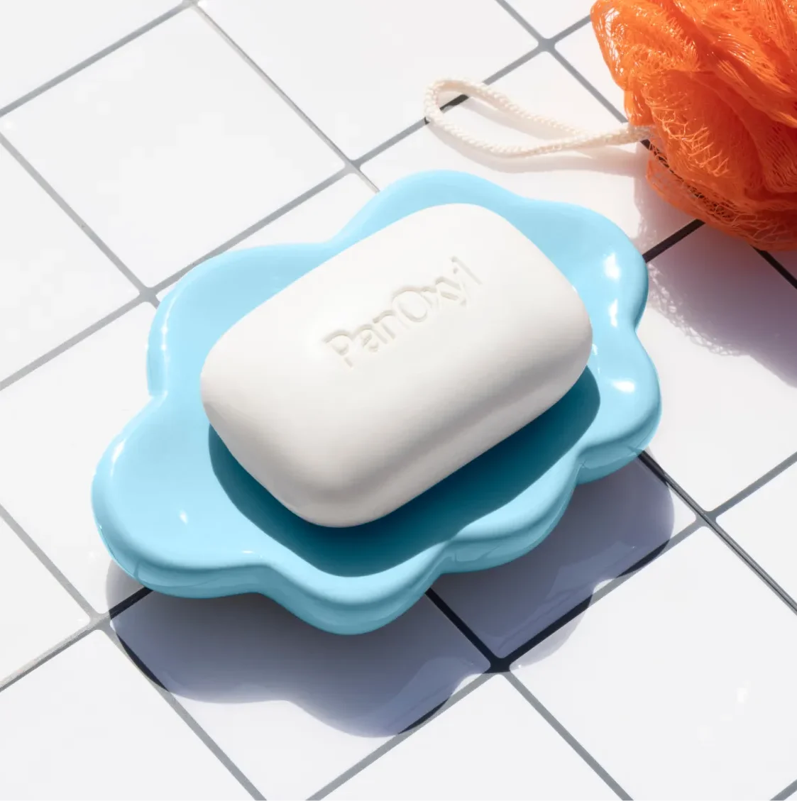 PanOxyl Acne Treatment Bar on a white tile background next to an orange loofah