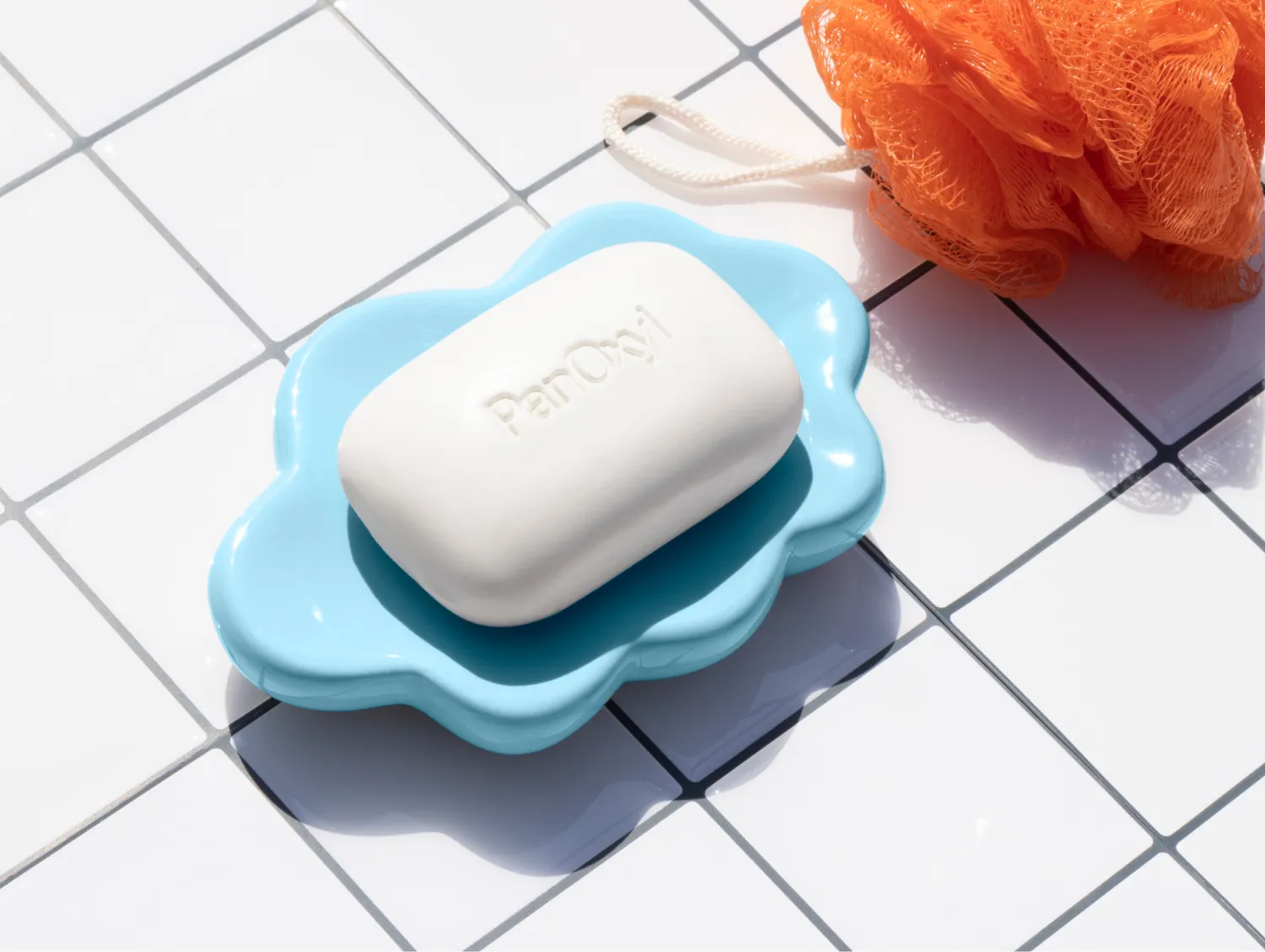 PanOxyl Acne Treatment Bar on a white tile background next to an orange loofah