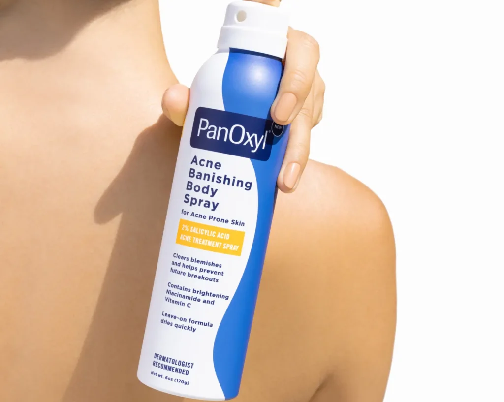 A person holding a bottle of PanOxyl Acne Banishing Body Spray over their back