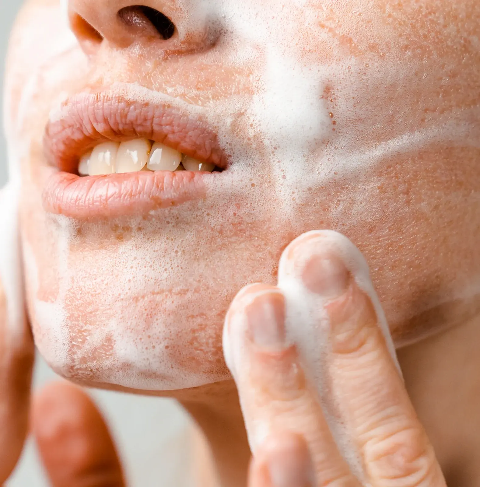 Close-up of a person washing their face with a foamy cleanser, focusing on their mouth and nose area.