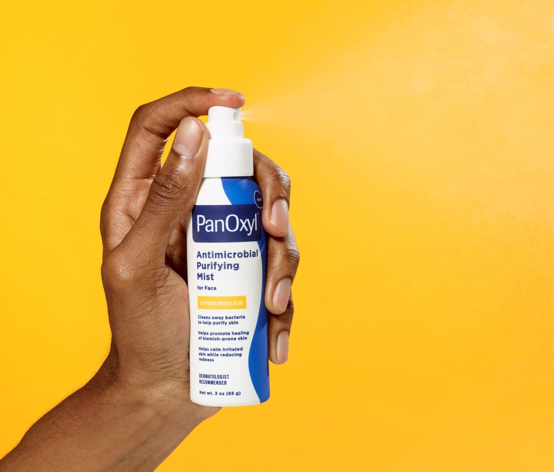 Hand spraying PanOxyl Antimicrobial Purifying mist bottle yellow background