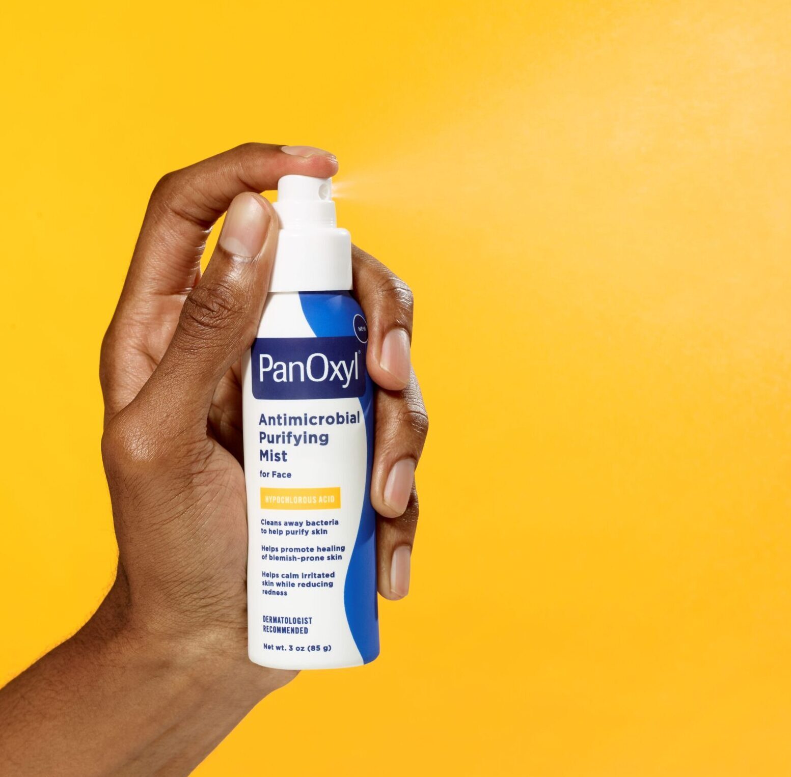 Hand spraying PanOxyl Antimicrobial Purifying mist bottle yellow background