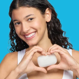 A smiling woman in a white top holding Hand holding PanOxyl Acne Cleansing bar on a blue background